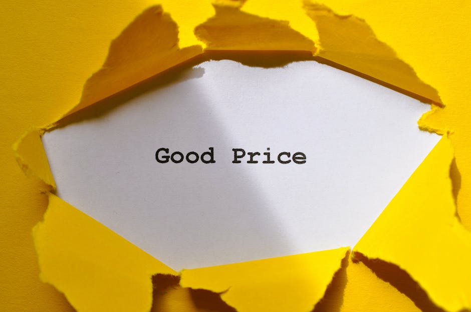 A white paper with the words 'Good Price' printed in black is visible through a rip in bright yellow paper or cardboard, creating a torn effect. The torn edges are irregular and frayed, revealing the message inside. The background appears to be a flat surface or wall, with the yellow material framing the quote. The scene suggests a focus on value or affordability, relevant in the context of home relocation, packing, and moving services offered by Man with Van Maryland. The lighting is even, ensuring the text is easily readable, while the torn yellow material emphasizes the idea of uncovering or revealing costs associated with removals and furniture transport.